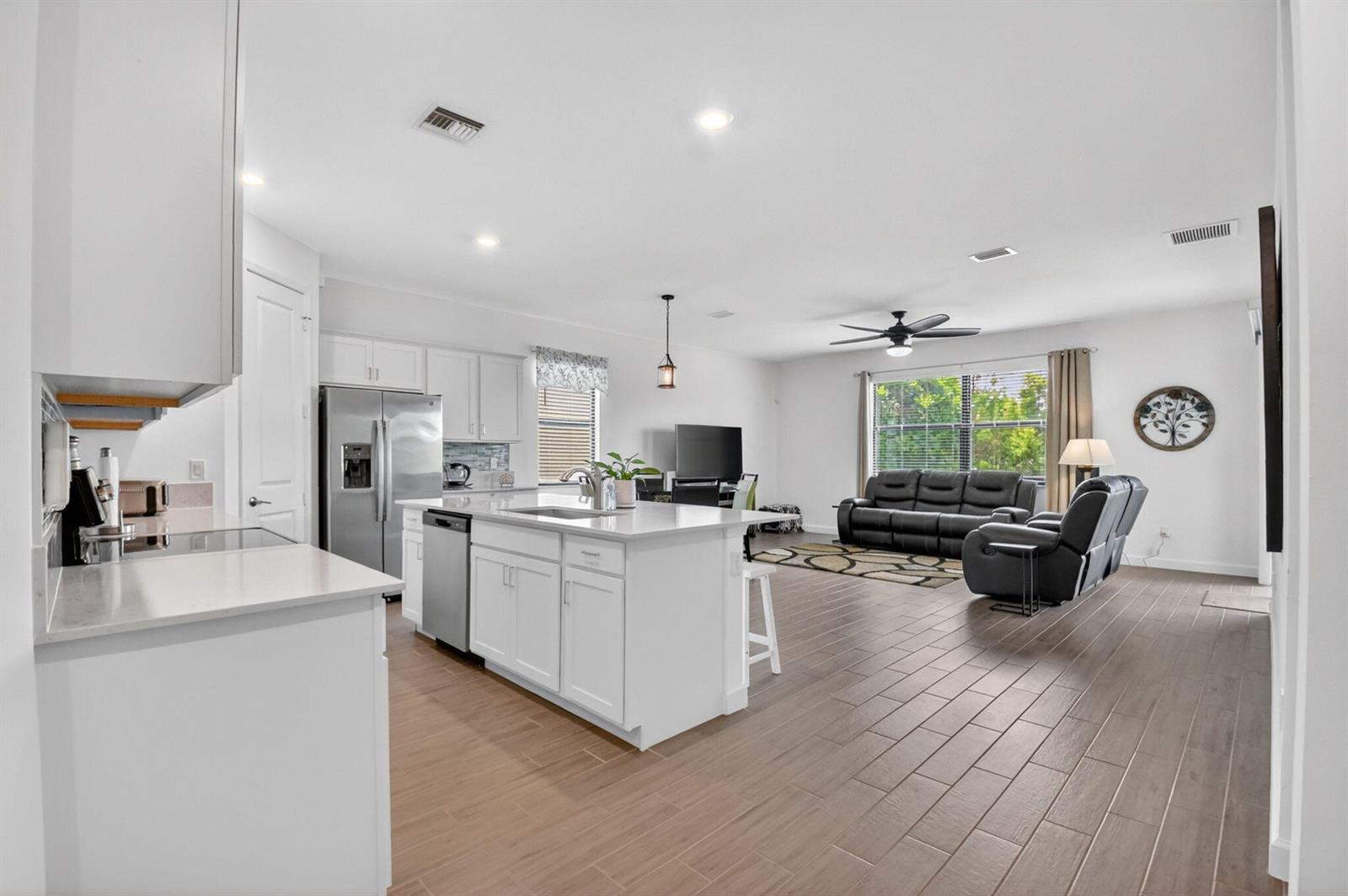 An open-concept kitchen with a white island and stainless appliances overlooks a living room area — 6026 Henderson Way, West Palm Beach FL 33415, WEST PALM BEACH, FL