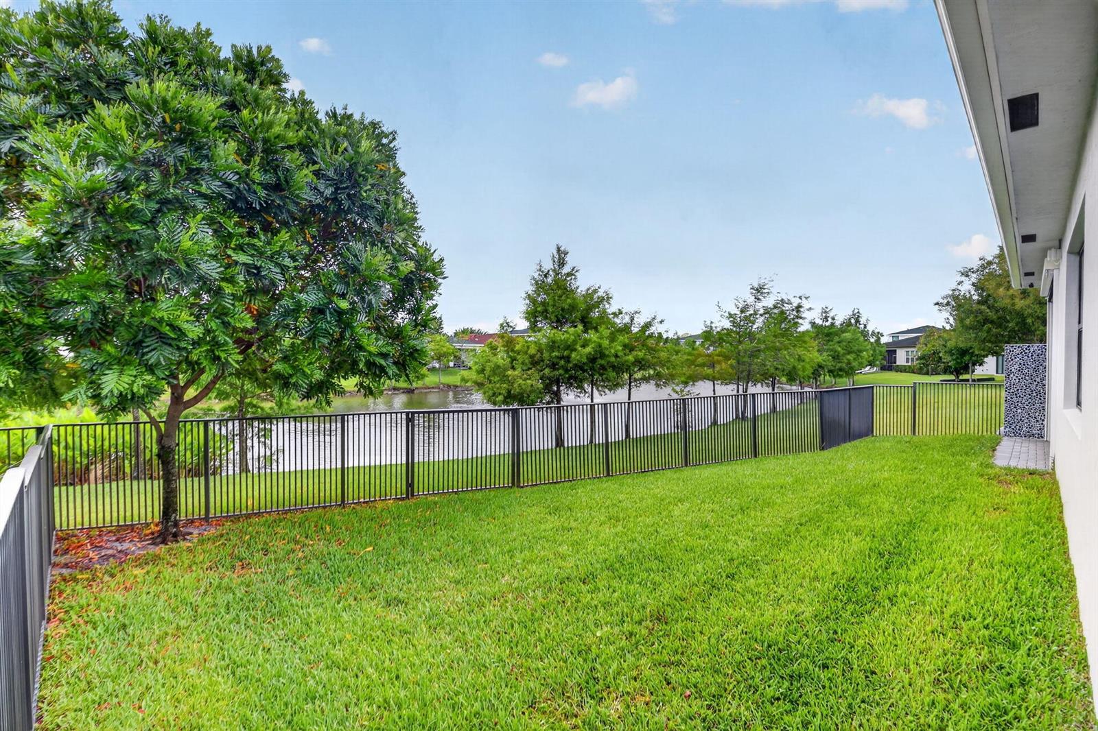 A backyard with a green lawn, a black metal fence, and a view of water — 6026 Henderson Way, West Palm Beach FL 33415, WEST PALM BEACH, FL