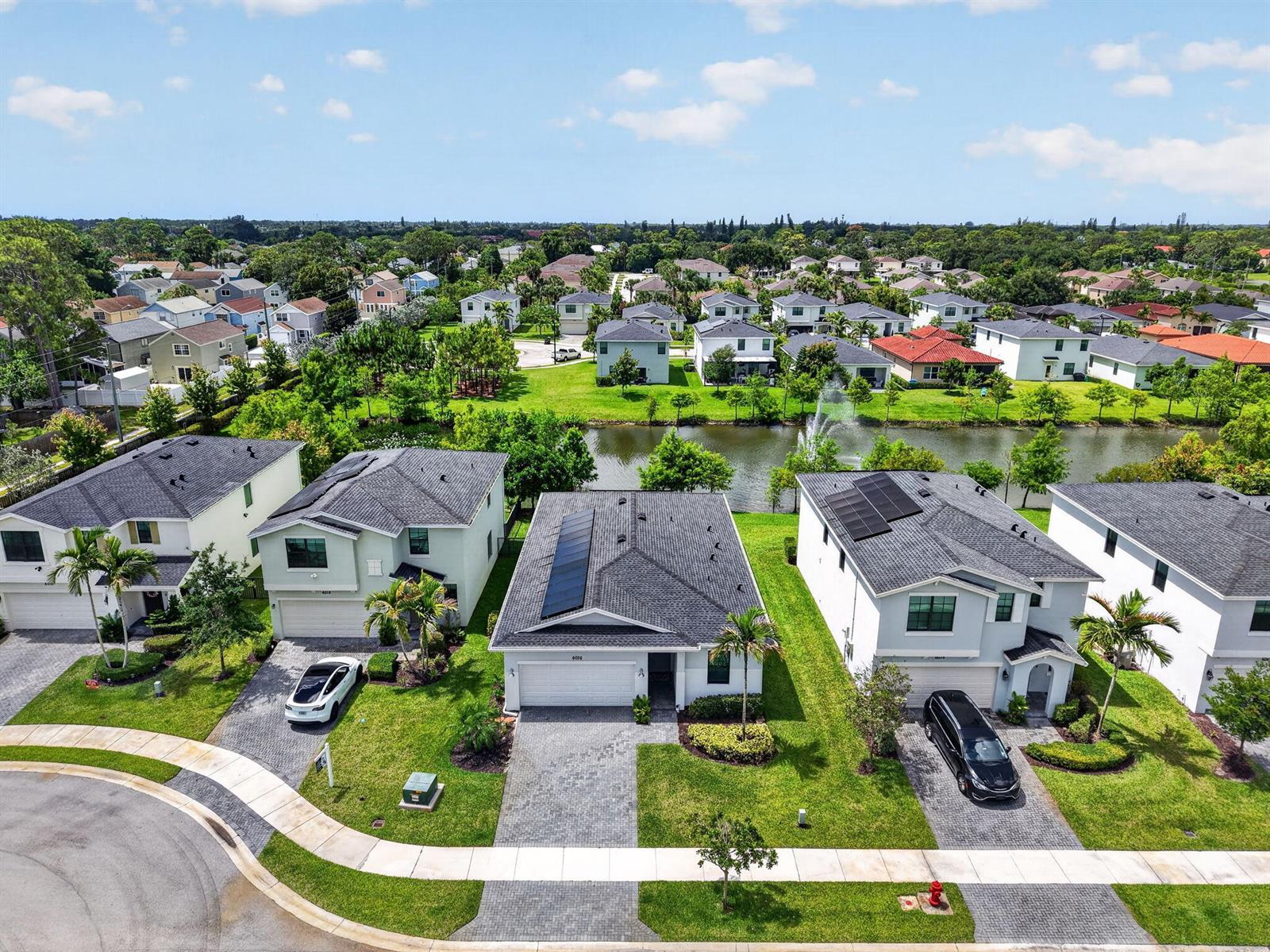 An aerial view of suburban houses with paved driveways and a central pond — 6026 Henderson Way, West Palm Beach FL 33415, WEST PALM BEACH, FL