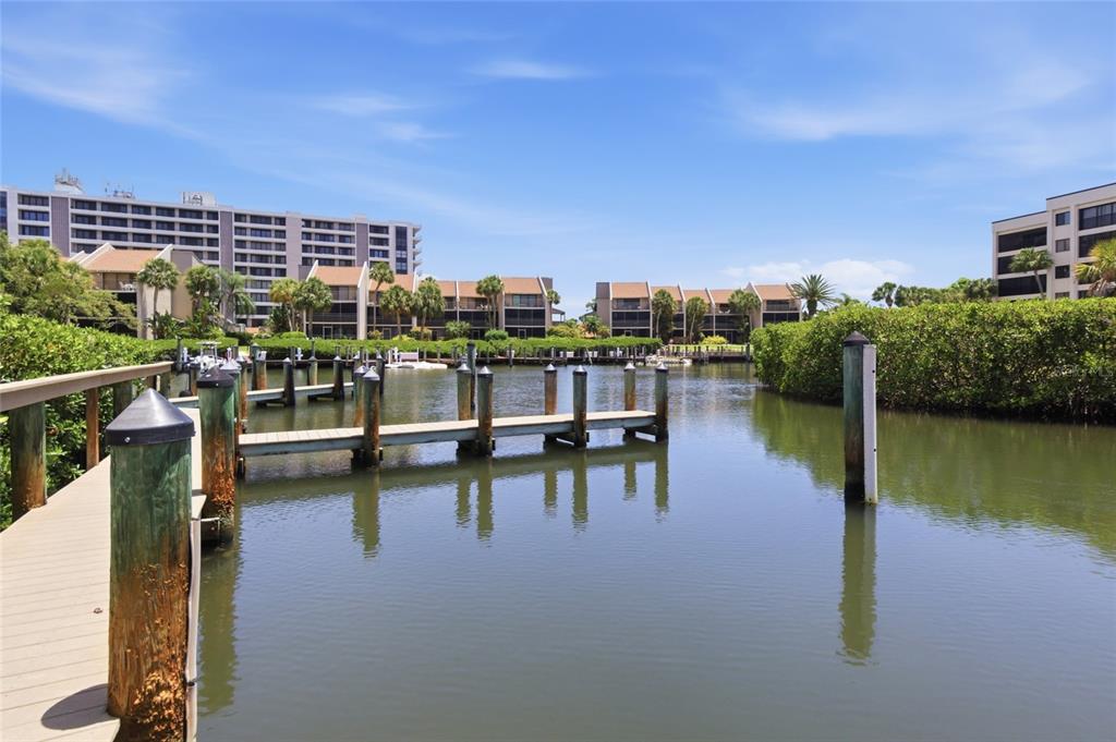 A wooden dock extends into a calm canal surrounded by lush vegetation and apartment buildings — 1500 COVE II PLACE UNIT 531, SARASOTA, FL