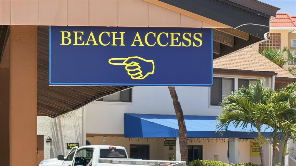 A blue sign with yellow text and a pointing hand indicates the direction to beach access — 1500 COVE II PLACE UNIT 531, SARASOTA, FL