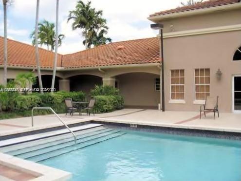 A swimming pool with steps sits in front of a tan building with a tiled roof — 18328 NW 68th Ave # H, Hialeah FL 33015, HIALEAH, FL