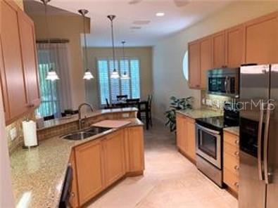 A kitchen with light wood cabinets, granite countertops, stainless steel appliances, and a breakfast bar — 7501 BOTANICA PARKWAY UNIT 202, SARASOTA, FL