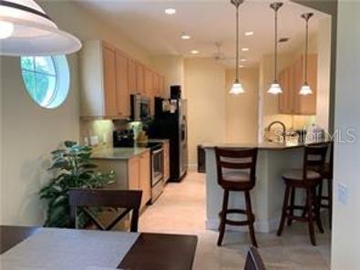 A kitchen with light wood cabinets, stainless steel appliances, and a breakfast bar with stools — 7501 BOTANICA PARKWAY UNIT 202, SARASOTA, FL