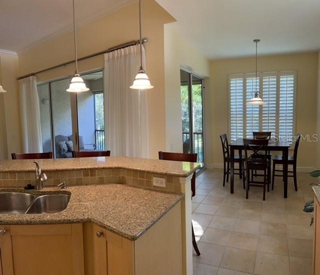 A kitchen with granite countertops and pendant lights overlooks a dining area with plantation shutters — 7501 BOTANICA PARKWAY UNIT 202, SARASOTA, FL