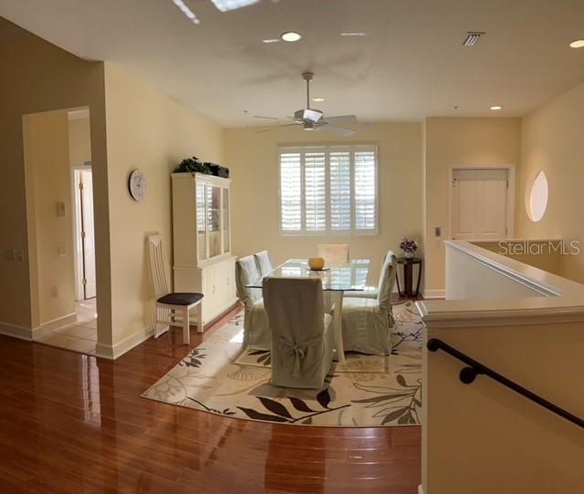 A dining room with a glass table, slipcovered chairs, a hutch, and hardwood floors — 7501 BOTANICA PARKWAY UNIT 202, SARASOTA, FL