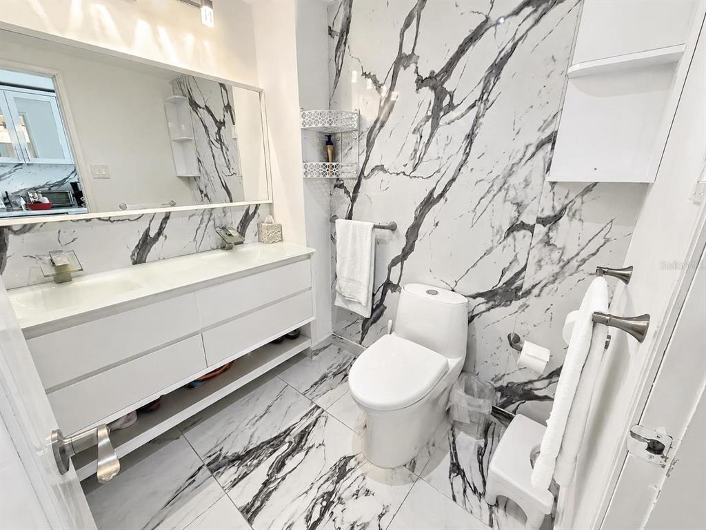 A bathroom features a white vanity, a toilet, and walls and floors with marble tile — 1 CALLE SAN GERONIMO UNIT 319, SAN JUAN, PR