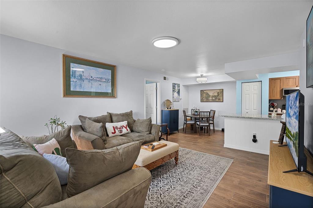 A living room with wood-look flooring, a gray sofa, and an adjacent dining area — 3028 PARKWAY BOULEVARD UNIT 308, KISSIMMEE, FL