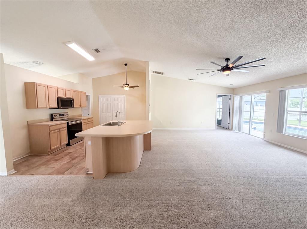 An open-concept kitchen with light wood cabinets and a breakfast bar overlooks a carpeted living area — 2366 BELEN DRIVE, DELTONA, FL