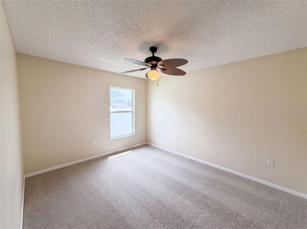 An empty bedroom features beige walls, tan carpet, and a ceiling fan with a light — 2366 BELEN DRIVE, DELTONA, FL