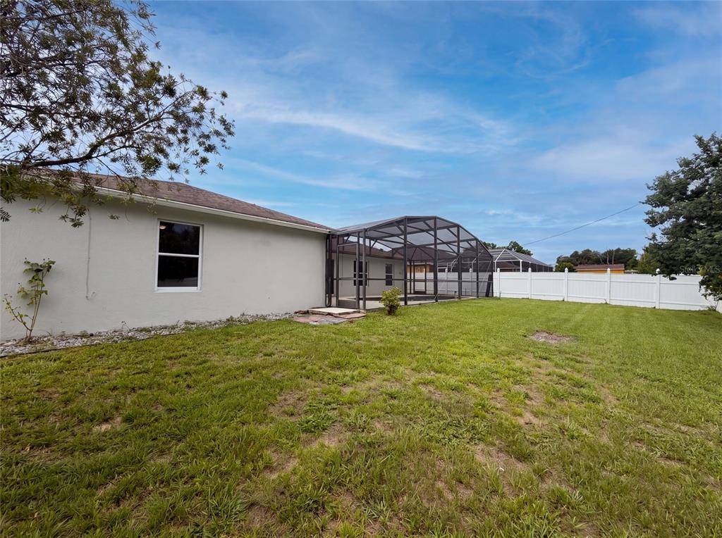 A backyard view of a house with a screened-in pool enclosure and a white fence — 2366 BELEN DRIVE, DELTONA, FL