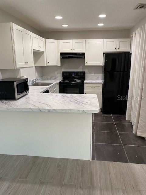 A kitchen features white cabinets, marble-patterned countertops, black appliances, and dark tile flooring — 165 WINDTREE LANE UNIT U, WINTER GARDEN, FL