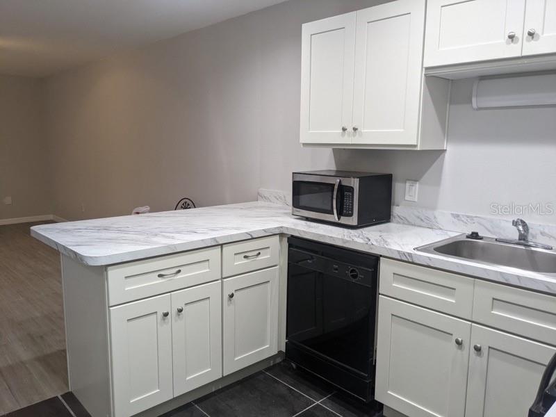 A kitchen features white cabinets, marble-patterned countertops, a black dishwasher, and a black microwave — 165 WINDTREE LANE UNIT U, WINTER GARDEN, FL