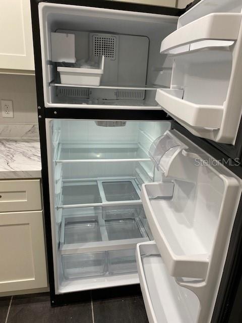 An open, empty top-freezer refrigerator stands in a kitchen with white cabinets and marble countertops — 165 WINDTREE LANE UNIT U, WINTER GARDEN, FL