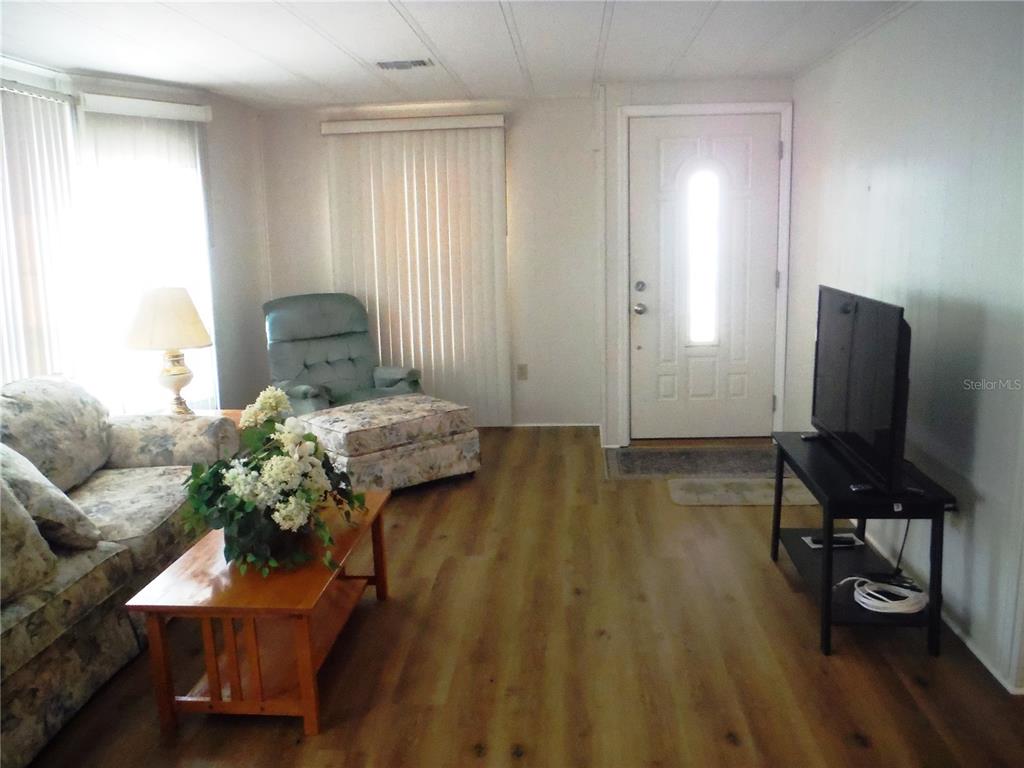 A living room features wood-look flooring, a floral sofa, a matching armchair, and a television — 141 FOREST LANE UNIT 13, SAFETY HARBOR, FL