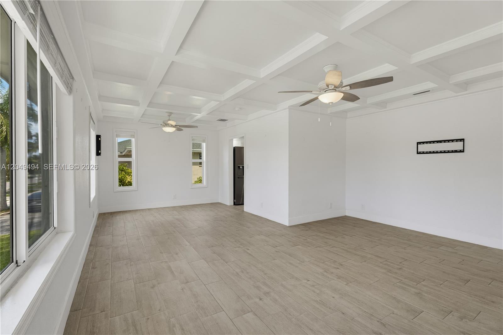 An empty room features white walls, a coffered ceiling, two ceiling fans, and wood-look flooring — 8020 SW 198th St, Cutler Bay FL 33189, CUTLER BAY, FL