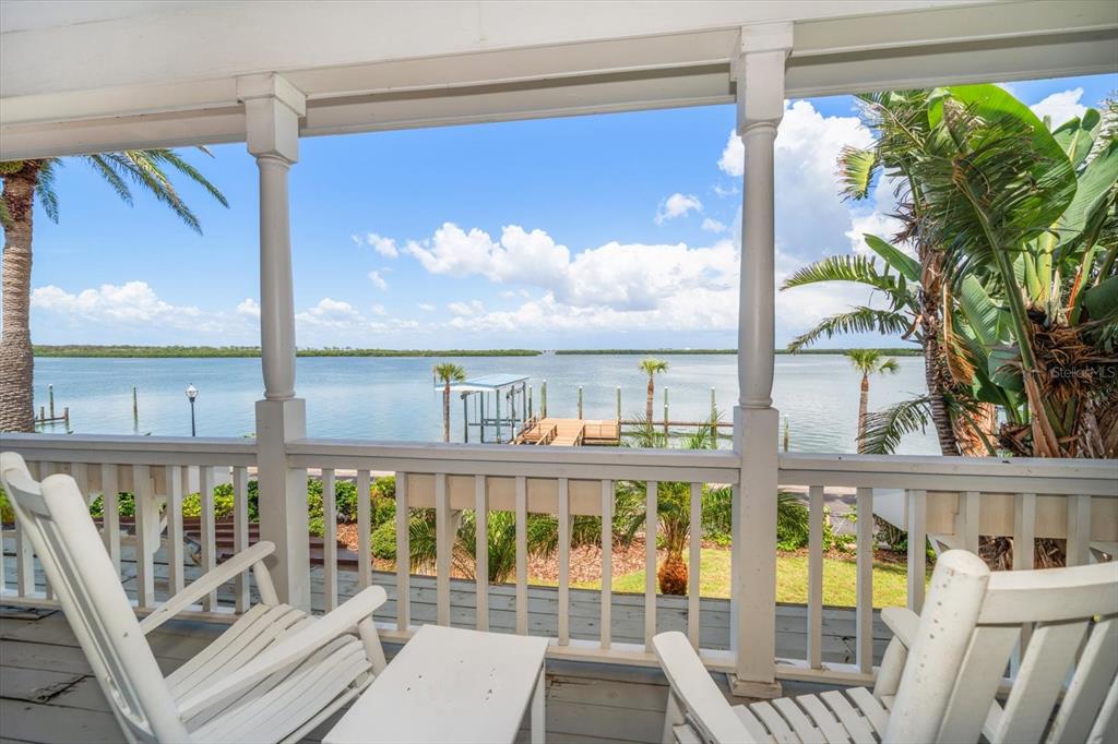 A wooden porch with two rocking chairs overlooks a calm bay and a private dock — 1114 MANDALAY POINT, CLEARWATER BEACH, FL