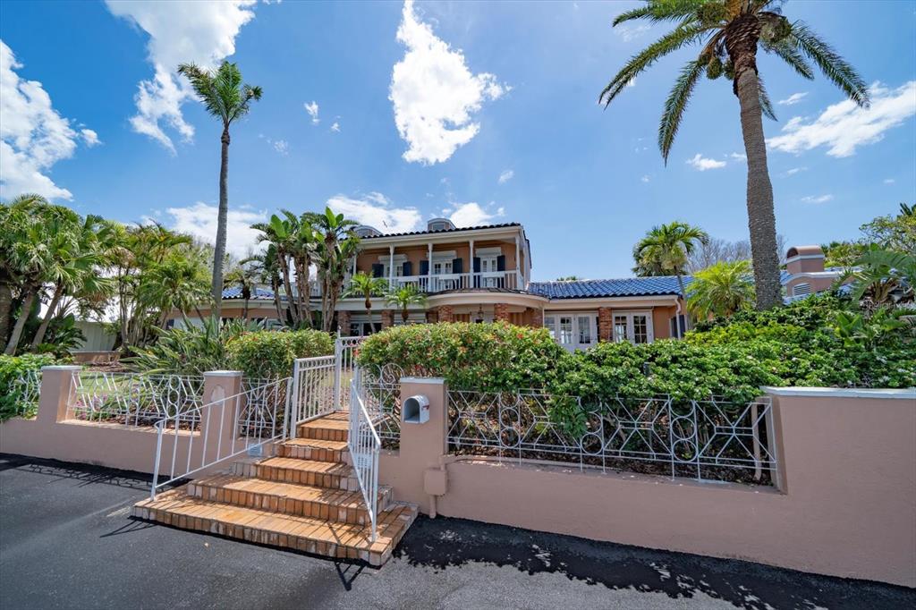 A two-story house with a blue tile roof, palm trees, and a gated brick staircase — 1114 MANDALAY POINT, CLEARWATER BEACH, FL