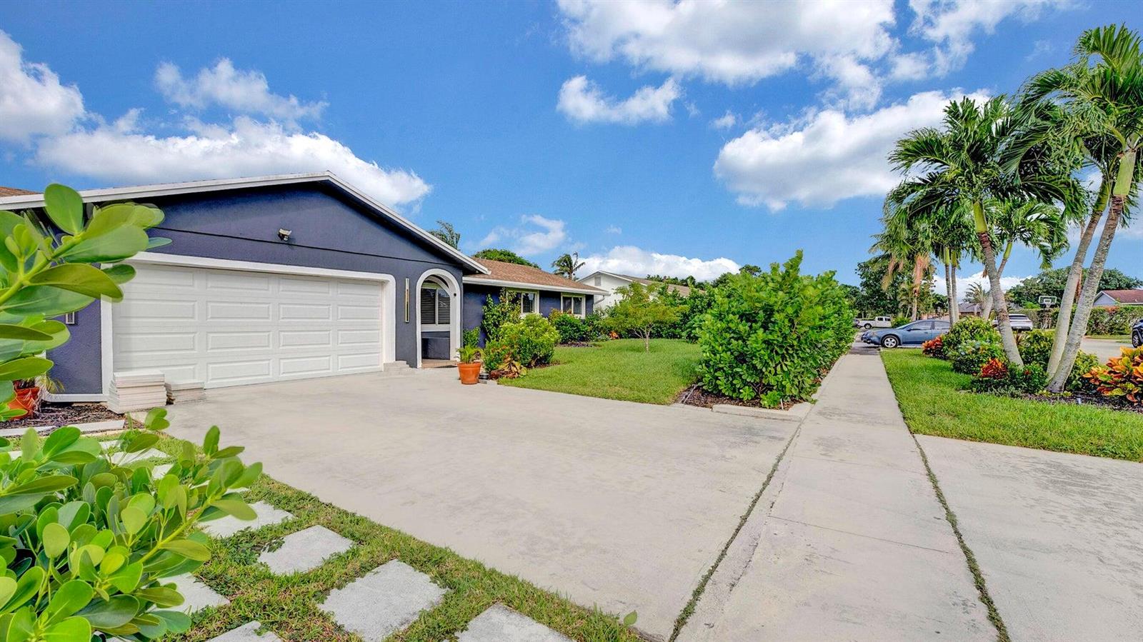 A blue house with a white garage door and a concrete driveway under a blue sky — 2941 Angler Drive, Delray Beach FL 33445, DELRAY BEACH, FL