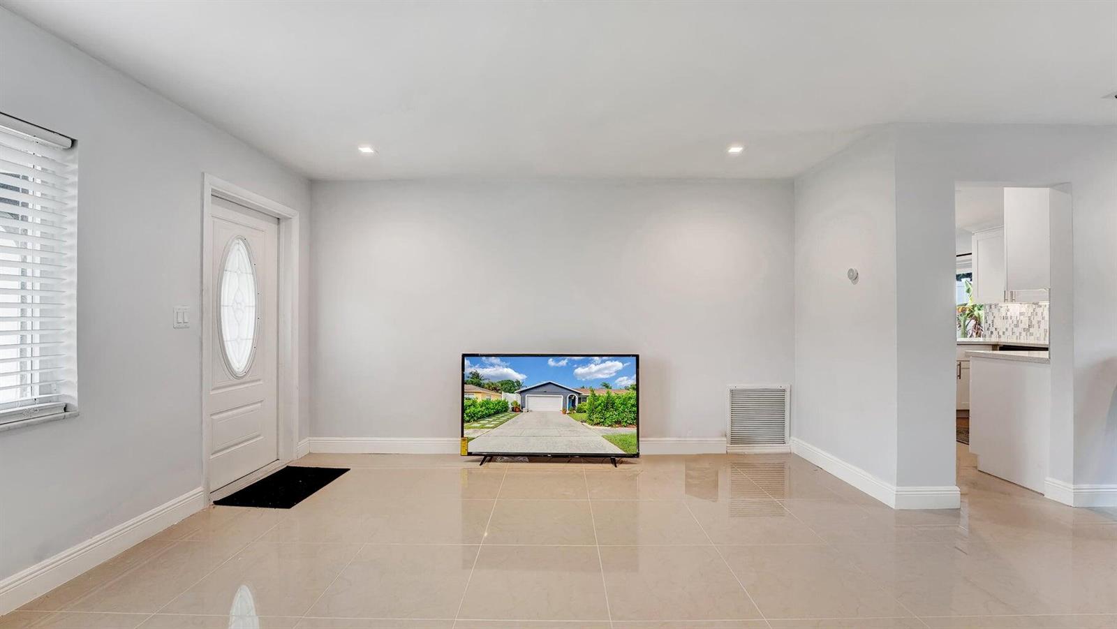 A living room with light-colored tile floors, a white front door, and a floor-standing television — 2941 Angler Drive, Delray Beach FL 33445, DELRAY BEACH, FL