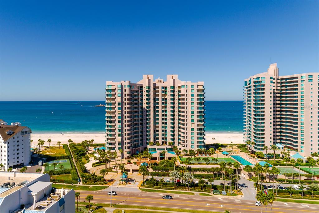 An aerial view shows high-rise beachfront condominiums with swimming pools and tennis courts — 1560 GULF BOULEVARD UNIT 1507, CLEARWATER BEACH, FL
