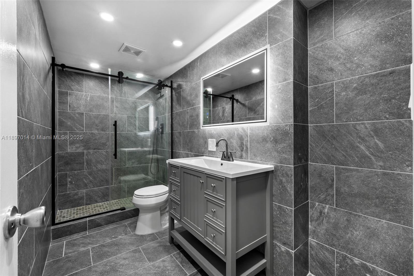 A modern bathroom features gray tile walls, a glass-enclosed shower, and a gray vanity — 401 Golden Isles Dr # 304, Hallandale Beach FL 33009, HALLANDALE BEACH, FL