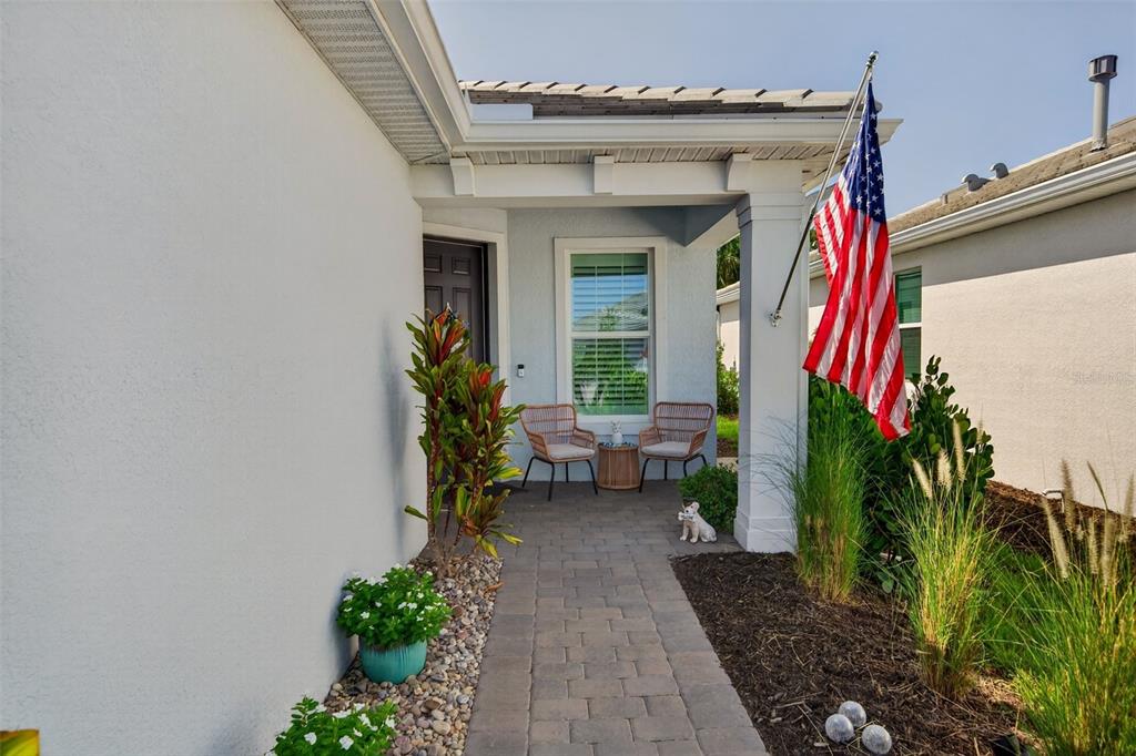 A paved walkway leads to a covered front porch with two chairs and an American flag — 10354 ABACO FALLS DRIVE, ENGLEWOOD, FL