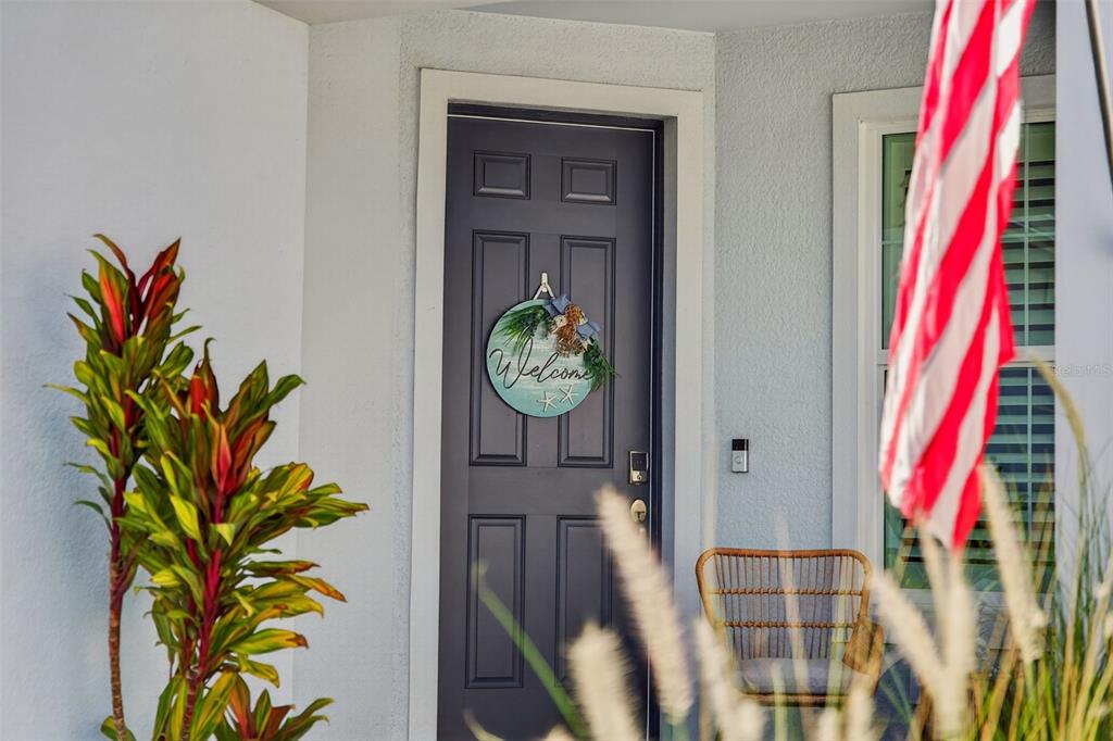 A dark blue front door with a welcome wreath sits on a porch with greenery — 10354 ABACO FALLS DRIVE, ENGLEWOOD, FL