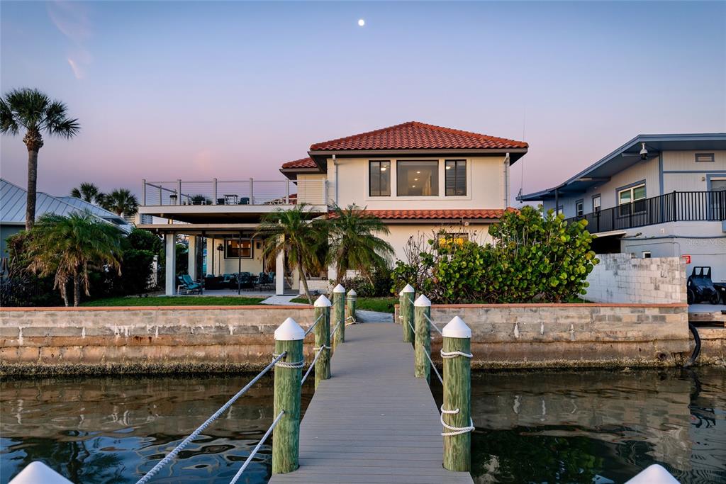 A waterfront house with a tiled roof, a wooden dock, and a large deck at sunset — 122 CORAL WAY, PORT ORANGE, FL