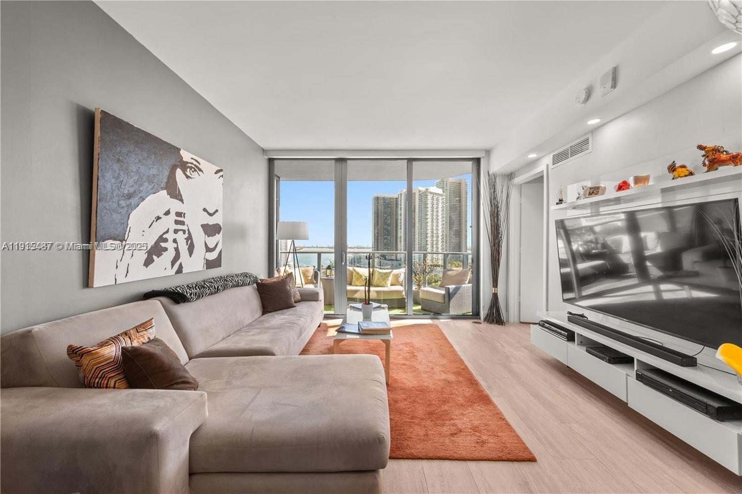 A living room features a large sectional sofa, a television, and a balcony with views — 121 NE 34th St # 1705, Miami FL 33137, MIAMI, FL