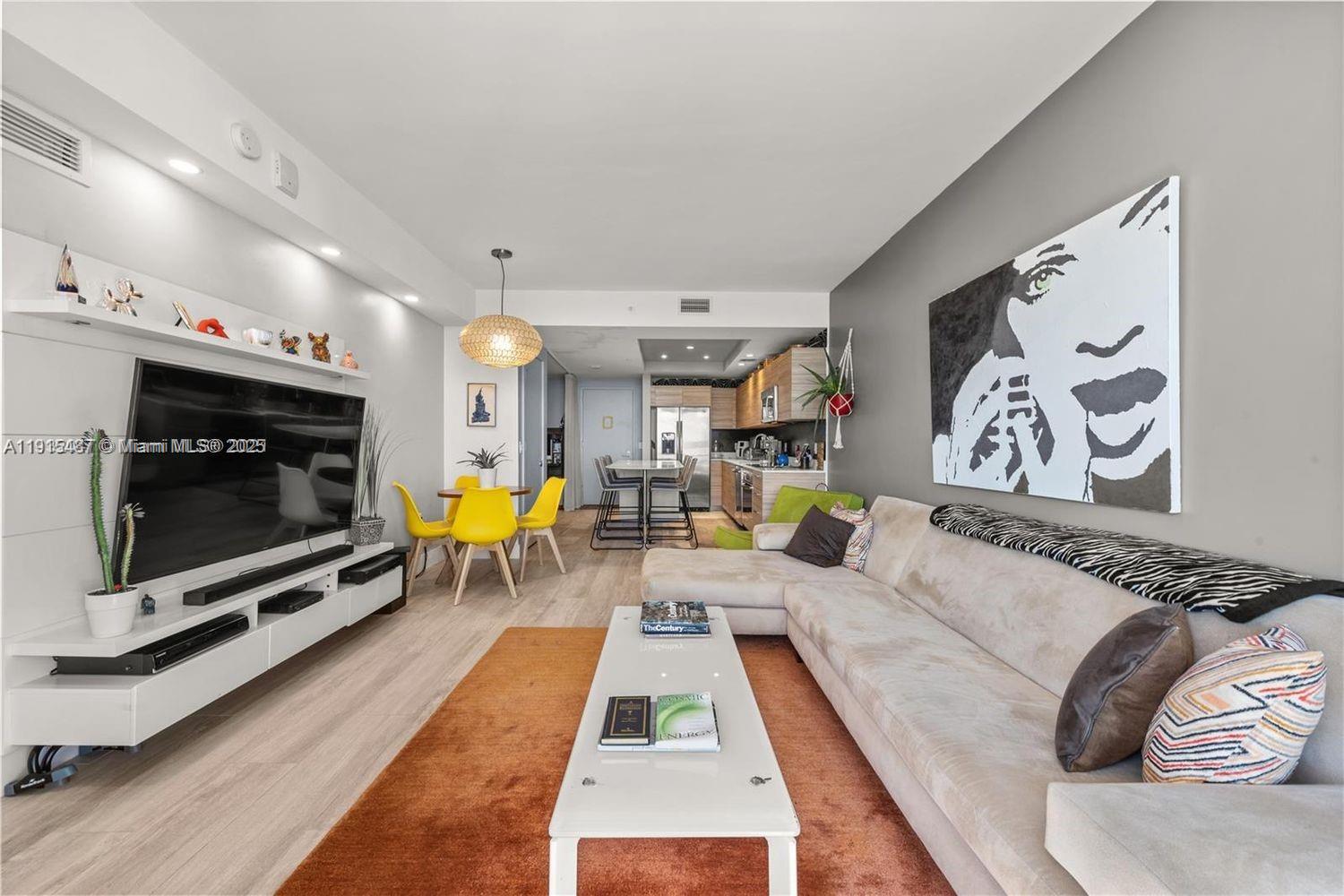 This living room features a large sectional sofa, a television, and an open-concept kitchen — 121 NE 34th St # 1705, Miami FL 33137, MIAMI, FL