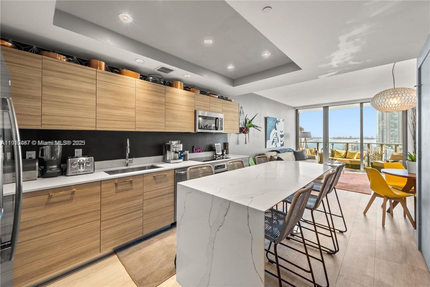 A modern kitchen features light wood cabinetry, a white marble island, and floor-to-ceiling windows — 121 NE 34th St # 1705, Miami FL 33137, MIAMI, FL