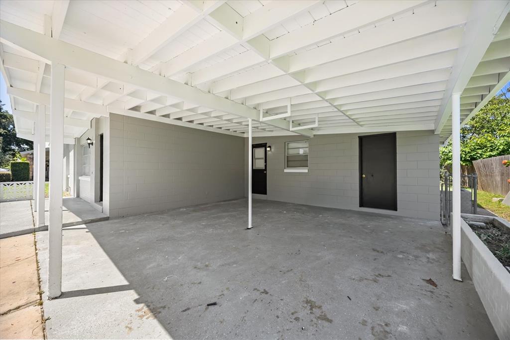 A covered concrete carport features a gray block wall and a white exposed beam ceiling — 1849 VIBURNUM LANE, WINTER PARK, FL