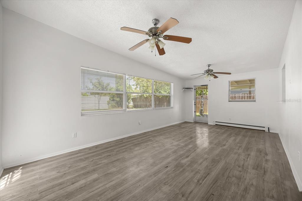 An empty room with light wood-look flooring, white walls, two ceiling fans, and large windows — 1849 VIBURNUM LANE, WINTER PARK, FL