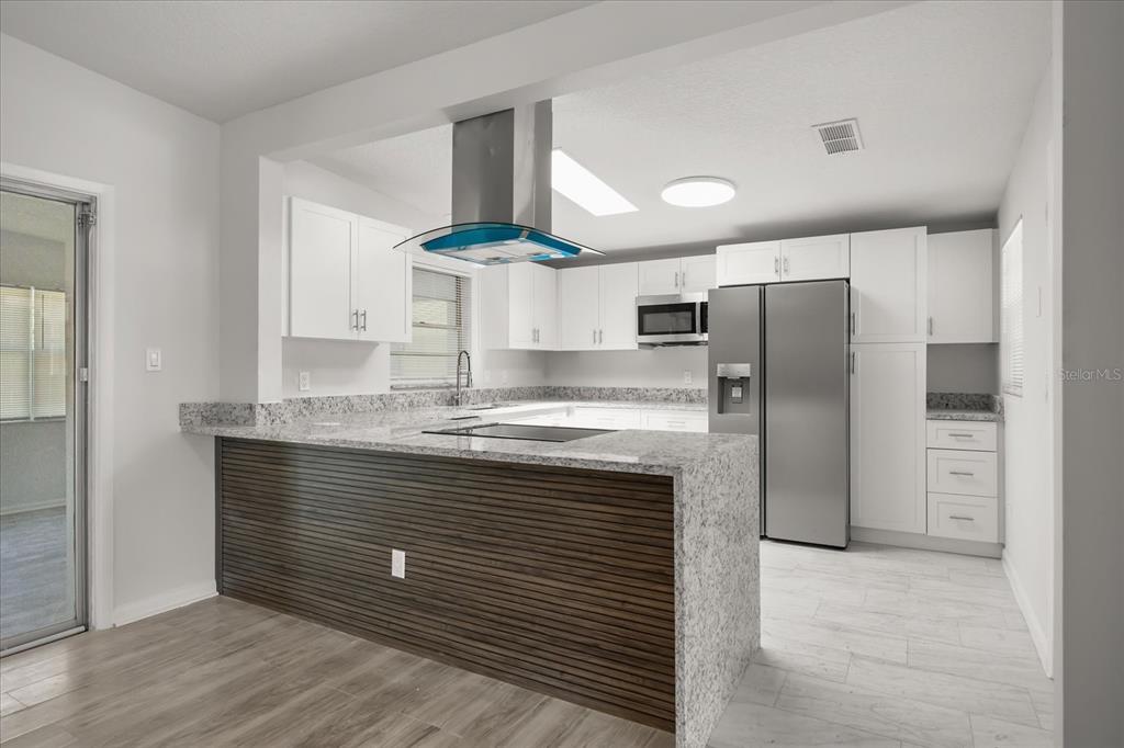A modern kitchen features white cabinets, granite countertops, a stainless steel refrigerator, and a wood-slatted island — 1849 VIBURNUM LANE, WINTER PARK, FL