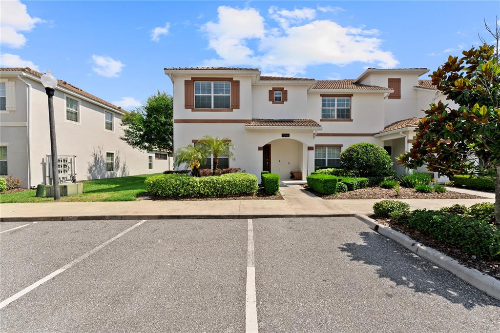 A two-story stucco townhouse with a tiled roof features a front entrance and parking lot — 1596 MOON VALLEY DRIVE, DAVENPORT, FL
