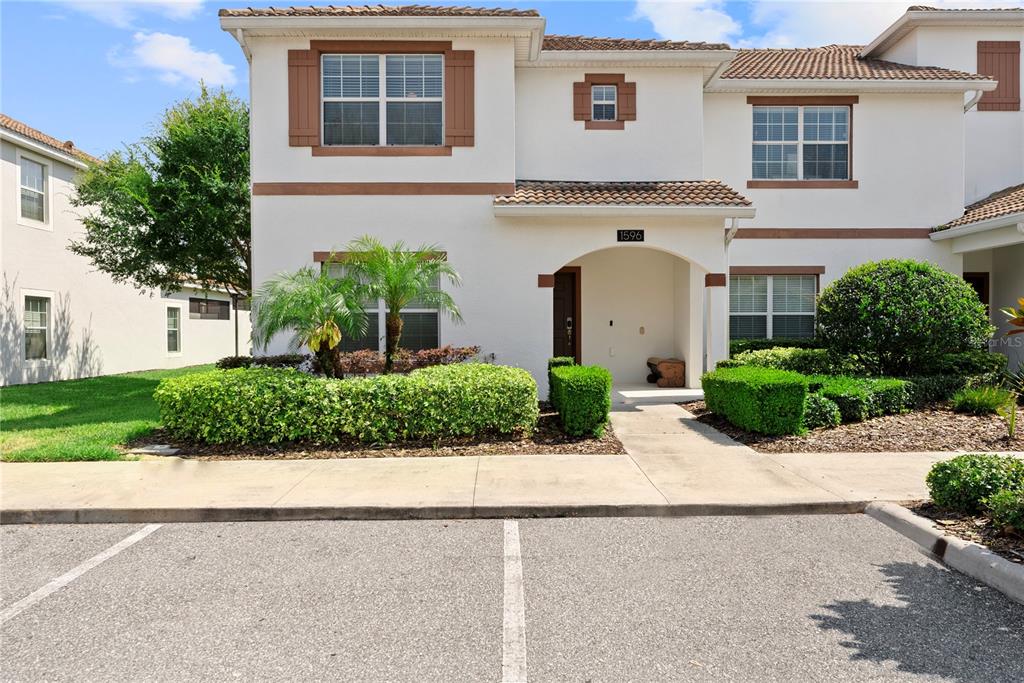 A two-story townhouse exterior features white stucco walls, brown shutters, and a tiled roof — 1596 MOON VALLEY DRIVE, DAVENPORT, FL