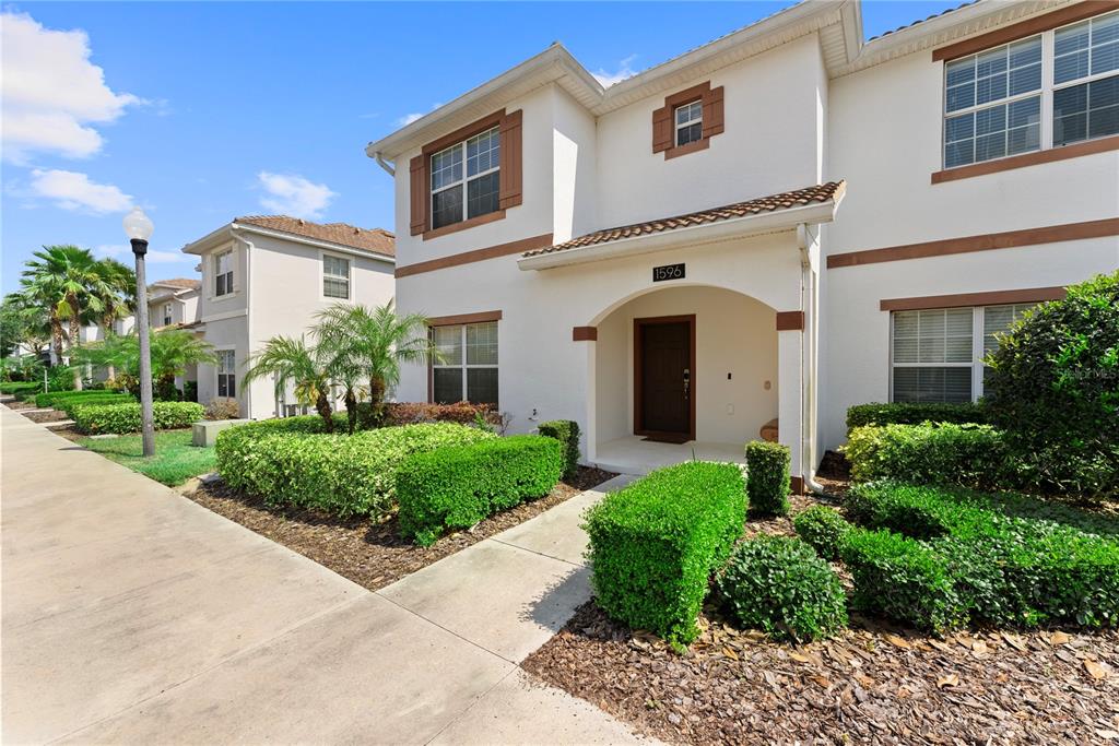 A two-story stucco townhouse with a brown front door and manicured hedges in the front — 1596 MOON VALLEY DRIVE, DAVENPORT, FL