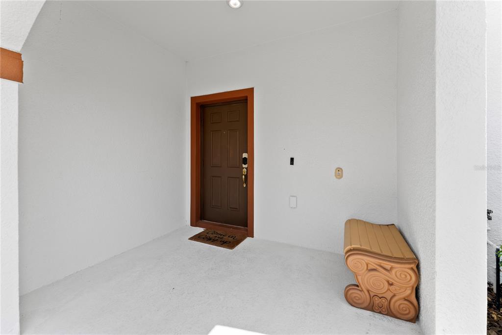 A covered entryway features a brown front door, a welcome mat, and a decorative bench — 1596 MOON VALLEY DRIVE, DAVENPORT, FL