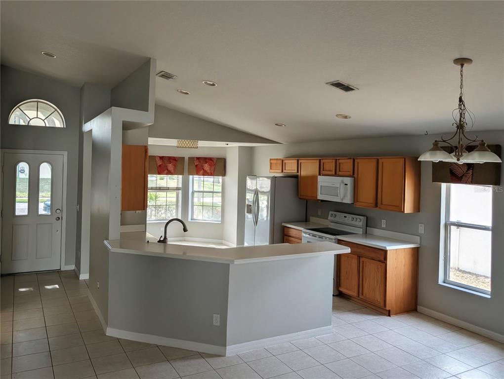 An open-concept kitchen features light gray walls, wood cabinets, white countertops, and tile flooring — 732 HENLEY CIRCLE, DAVENPORT, FL