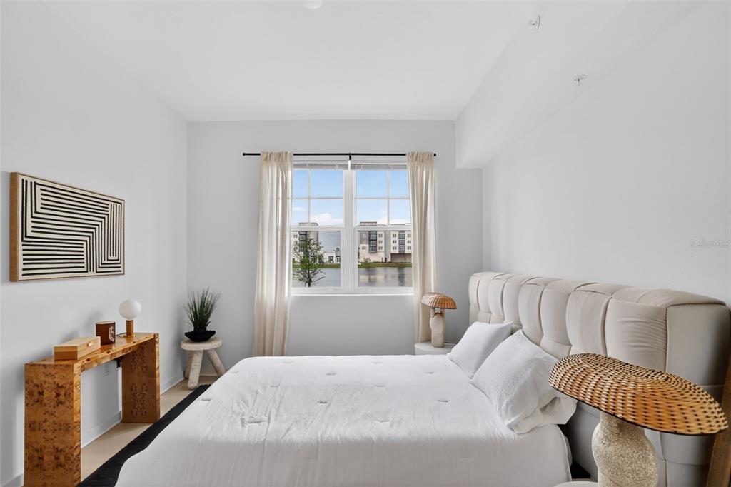 A bedroom features a tufted headboard, a burl wood console table, and a window view — 5579 MILLENIA PARK BOULEVARD UNIT 523, ORLANDO, FL