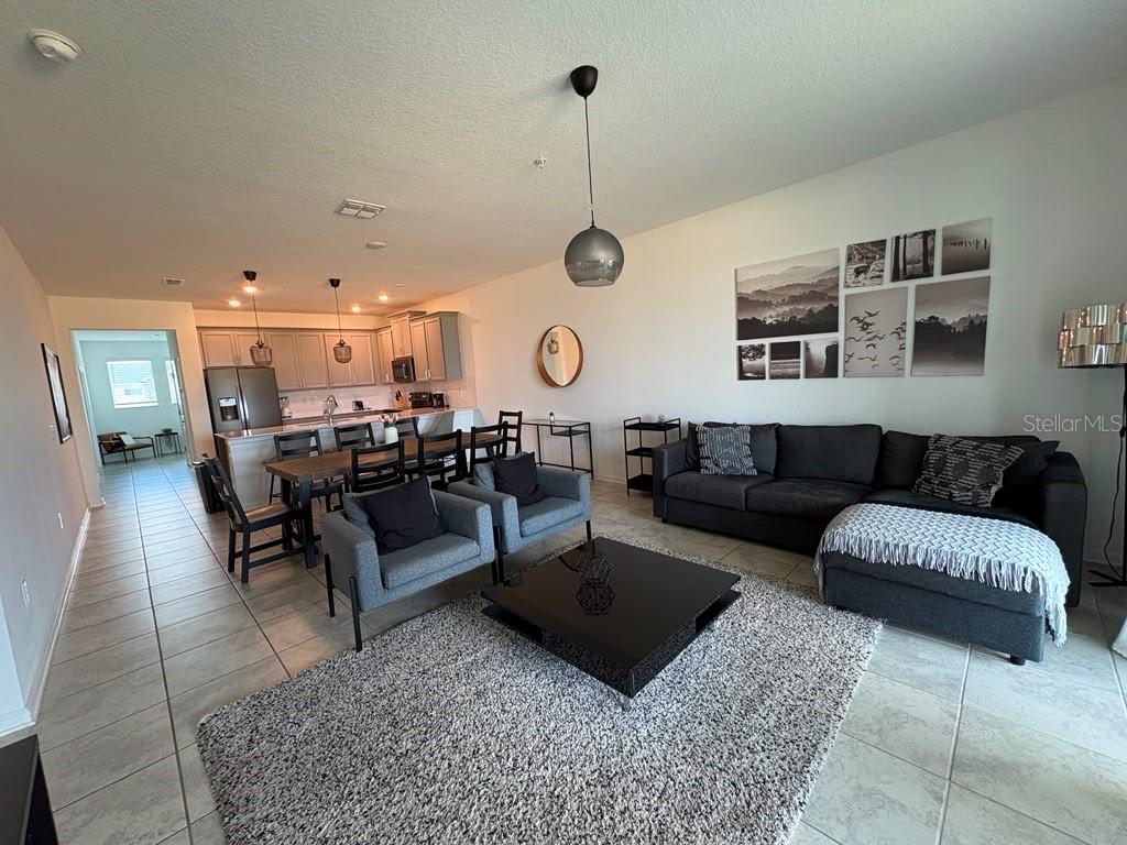 An open-concept living and dining area features a gray sectional, dining table, and kitchen island — 993 SPLASH SHOT PLACE, DAVENPORT, FL