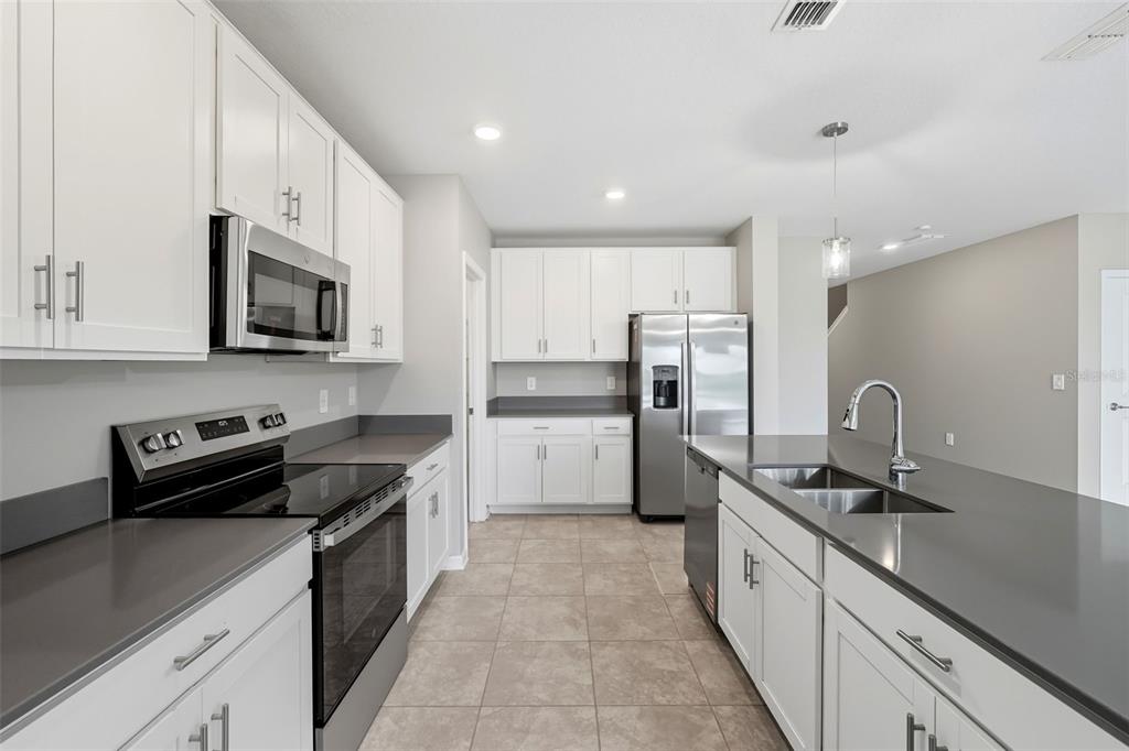 A modern kitchen features white cabinets, stainless steel appliances, and dark gray countertops — 724 DARING DRIVE, DAVENPORT, FL