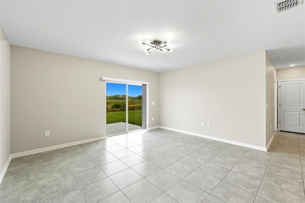 A bright, empty room features light gray tile flooring, beige walls, and a sliding glass door — 724 DARING DRIVE, DAVENPORT, FL