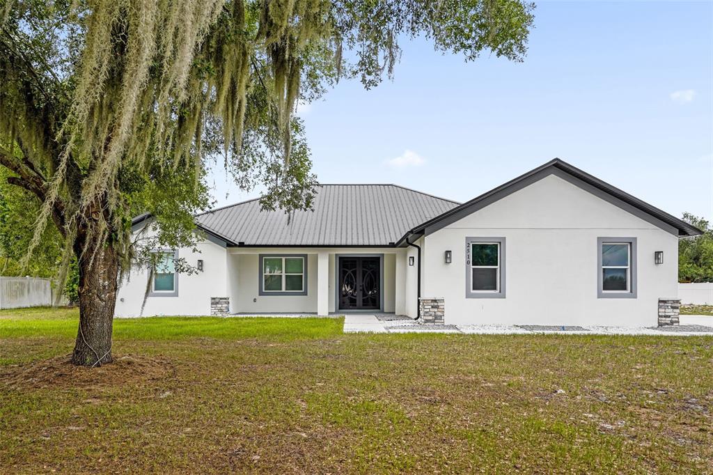 A single-story white house with a metal roof sits behind a large mossy tree — 2510 LAKE FRONT DRIVE, LAKE WALES, FL
