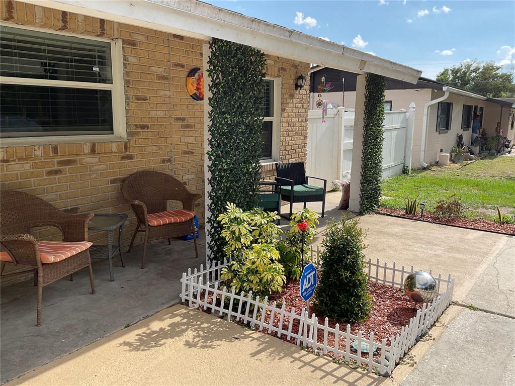 A brick house exterior features a covered patio with wicker chairs and a small garden — 837 CAMPELLO STREET, ALTAMONTE SPRINGS, FL