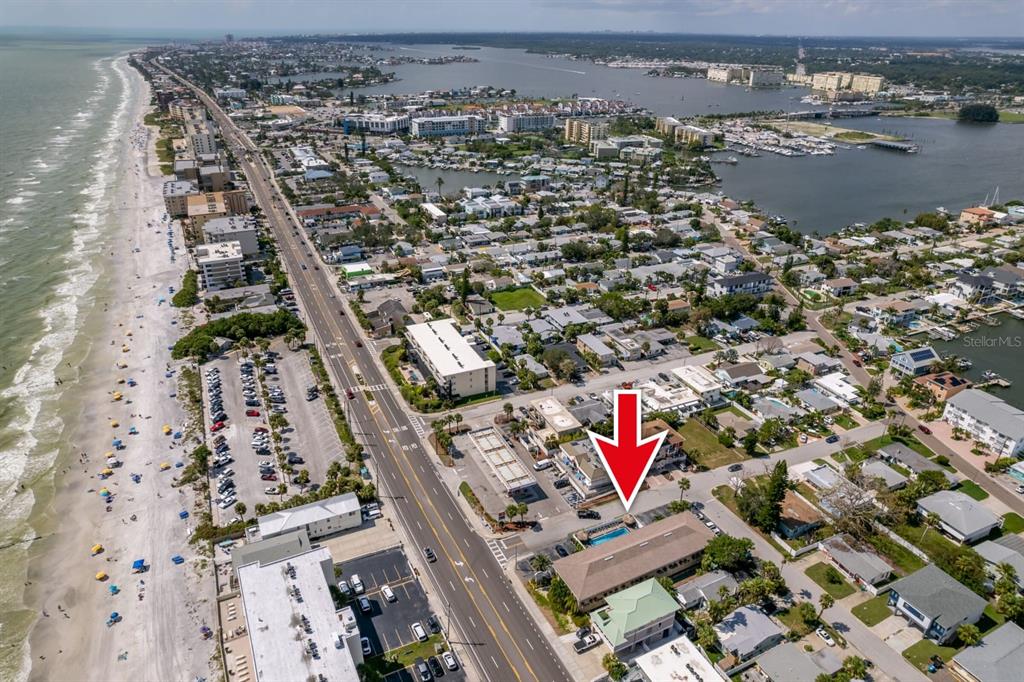 An aerial view shows a coastal neighborhood with a beach, road, and buildings — 14251 GULF BOULEVARD UNIT 12, ST PETERSBURG, FL
