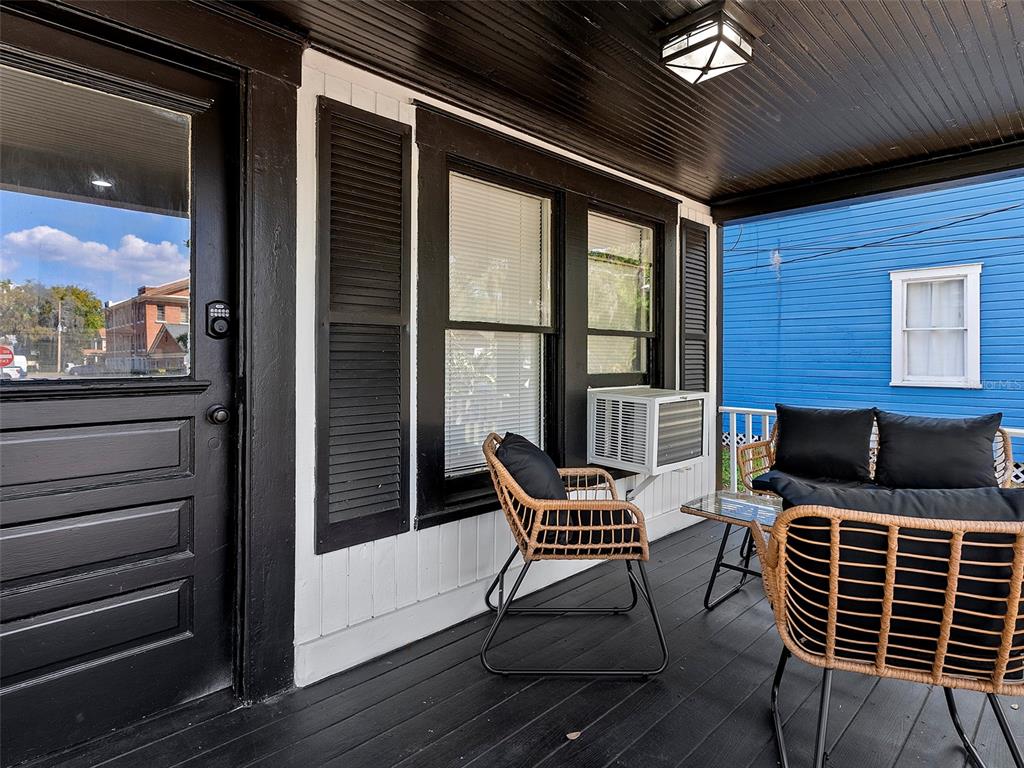 A covered porch features black trim, wicker chairs with black cushions, and a window air conditioner — 412 E HARWOOD STREET UNIT 1, ORLANDO, FL