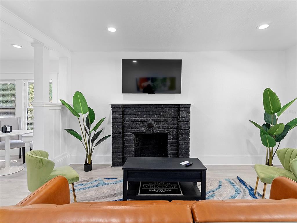 A living room features a black brick fireplace, a mounted television, and two potted plants — 412 E HARWOOD STREET UNIT 1, ORLANDO, FL