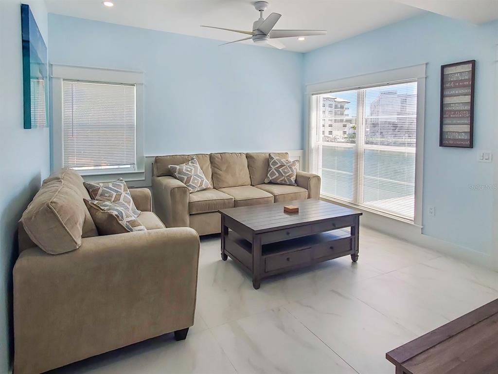 A living room features light blue walls, beige sofas, a wooden coffee table, and water views — 215 MEDALLION BOULEVARD UNIT G, MADEIRA BEACH, FL